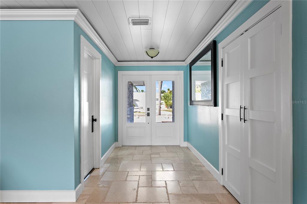 A bright entryway features light blue walls, a white plank ceiling, and stone tile flooring — 10038 S YACHT CLUB DRIVE, TREASURE ISLAND, FL