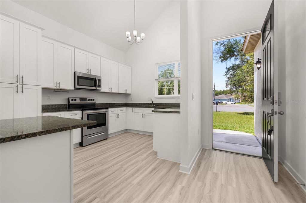 A kitchen with white cabinets, granite countertops, stainless steel appliances, and an open exterior door — 713 SWALLOW LANE, POINCIANA, FL