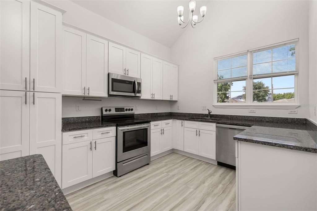 A kitchen with white cabinets, stainless steel appliances, and dark granite countertops — 713 SWALLOW LANE, POINCIANA, FL