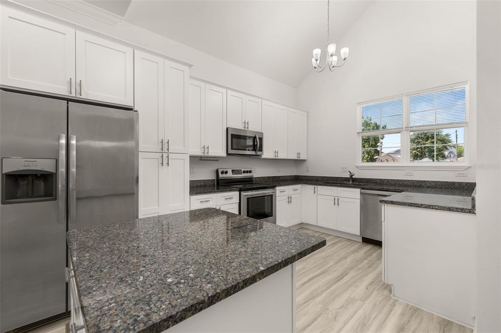A kitchen features white cabinetry, granite countertops, stainless steel appliances, and a vaulted ceiling — 713 SWALLOW LANE, POINCIANA, FL