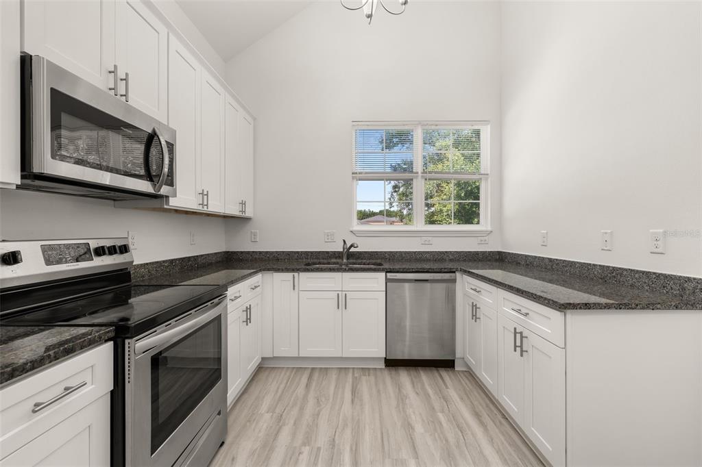 A kitchen with white cabinets, granite countertops, stainless steel appliances, and light wood-look flooring — 713 SWALLOW LANE, POINCIANA, FL