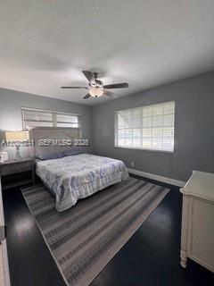 A bedroom features a bed with a patterned quilt, a ceiling fan, and dark flooring — FORT LAUDERDALE, FL