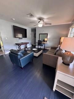 A living room with dark flooring, a blue armchair, a sofa, and a wall-mounted television — FORT LAUDERDALE, FL