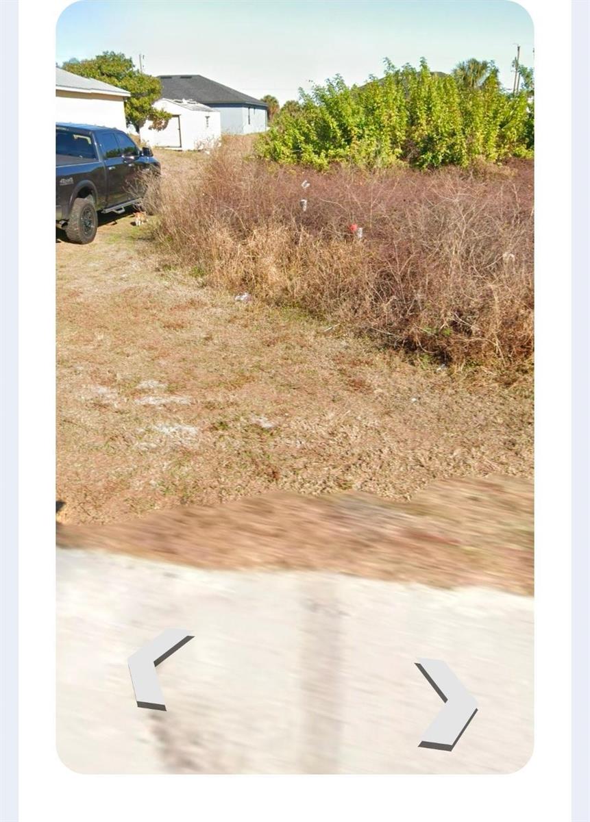 A view of a vacant, overgrown lot next to a parked truck and a house — 819 E Casper Yost Street E, Lehigh Acres FL 33974, LEHIGH ACRES, FL