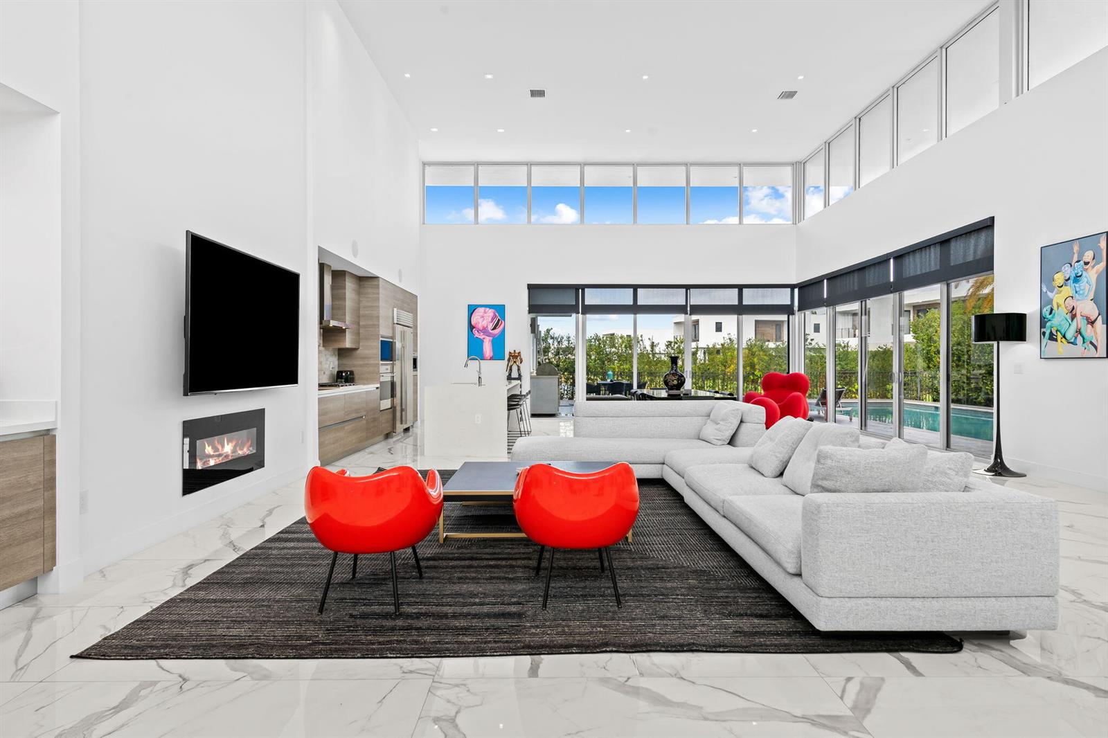 A modern, high-ceilinged living room features a white sectional, red accent chairs, and a fireplace — 16758 Natures Way, Weston FL 33326, WESTON, FL