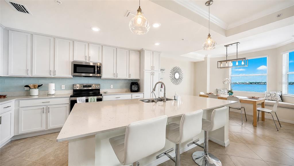 A bright kitchen features white cabinetry, a large quartz island, and a dining nook overlooking water — 1020 TIDEWATER SHORES LOOP UNIT 207, BRADENTON, FL