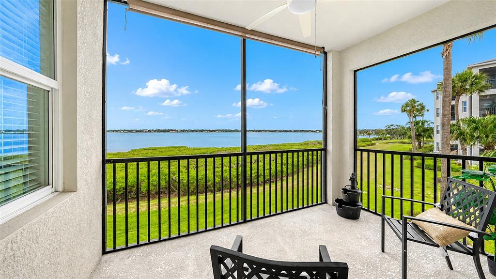 A screened-in balcony overlooks a grassy lawn, palm trees, and a large body of water — 1020 TIDEWATER SHORES LOOP UNIT 207, BRADENTON, FL