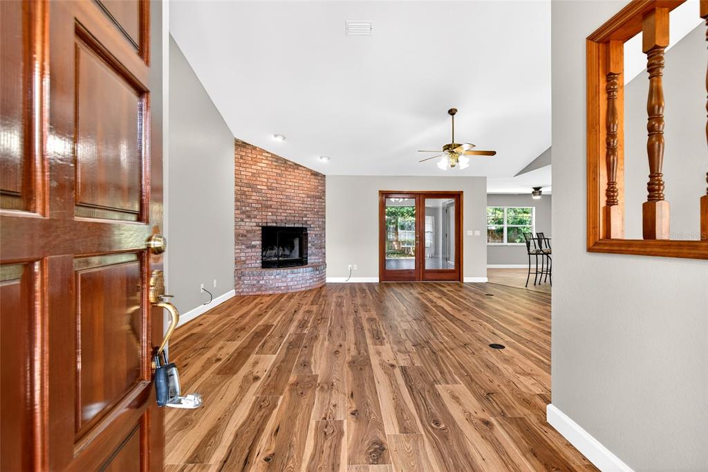 A view from an open doorway into a living room with wood flooring and brick fireplace — 5393 SW 86TH PLACE, OCALA, FL