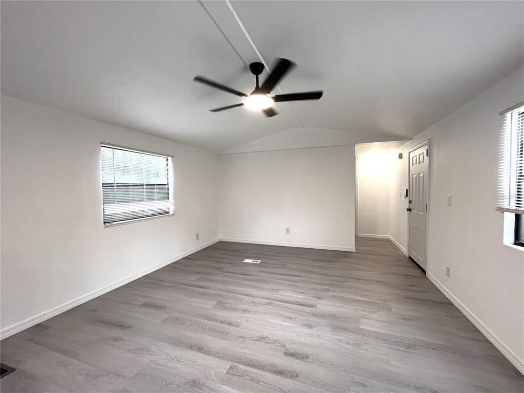 A bright, empty room features white walls, gray wood-look flooring, and a ceiling fan — 9860 GOLDEN LOOP, NEW PORT RICHEY, FL