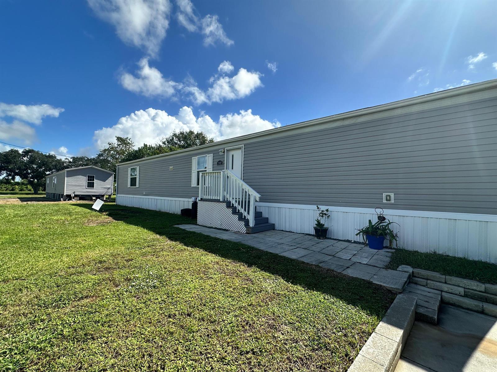 A gray manufactured home features white stairs, a stone walkway, and a grassy yard — 5945 SE 95th Trail Trail, Okeechobee FL 34974, OKEECHOBEE, FL