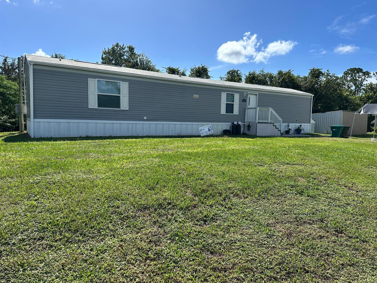 A single-story manufactured home with gray siding sits on a large, grassy lot — 5945 SE 95th Trail Trail, Okeechobee FL 34974, OKEECHOBEE, FL