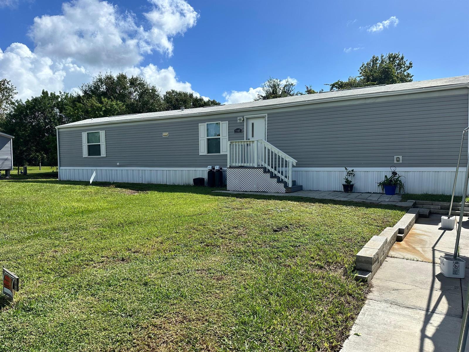 A gray manufactured home with white trim and a small front porch sits on grass — 5945 SE 95th Trail Trail, Okeechobee FL 34974, OKEECHOBEE, FL