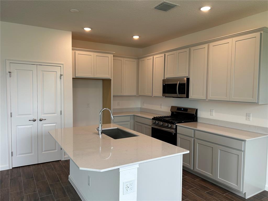 A kitchen with light gray cabinets, a quartz-topped island, and dark wood-look tile flooring — 2256 SIRENA LANE, MOUNT DORA, FL