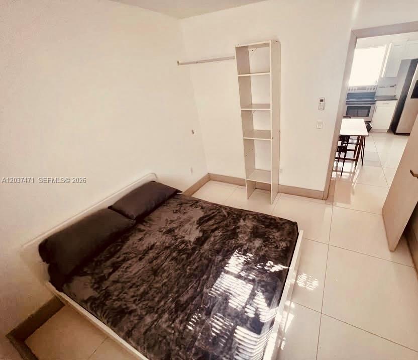 A bedroom with a bed, a tall shelving unit, and a view into a kitchen — 1145 NW 28th St # B, Miami FL 33127, MIAMI, FL