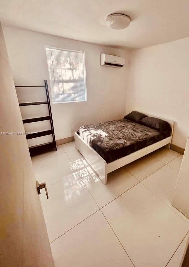 A bedroom with white tile floors, a bed, a window, and a wall-mounted air conditioner — 1145 NW 28th St # B, Miami FL 33127, MIAMI, FL