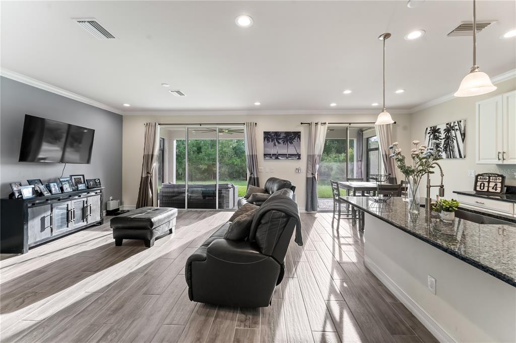 A living room and kitchen area with tile floors, dark leather furniture, and sliding glass doors — 1295 MONTGOMERY BELL ROAD, WESLEY CHAPEL, FL