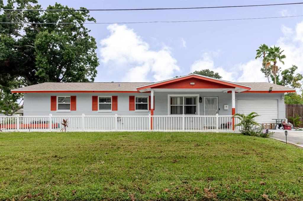 A single-story house with gray siding, orange trim, and a white picket fence — 7200 8TH STREET N, ST PETERSBURG, FL