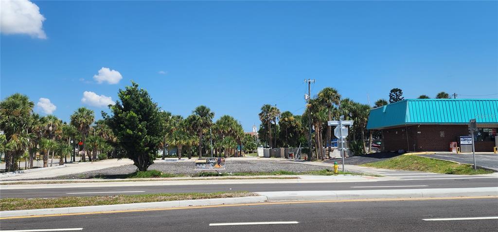 A vacant, gravel-covered lot sits next to a brick building with a teal roof — E INTERNATIONAL SPEEDWAY BOULEVARD, DAYTONA BEACH, FL