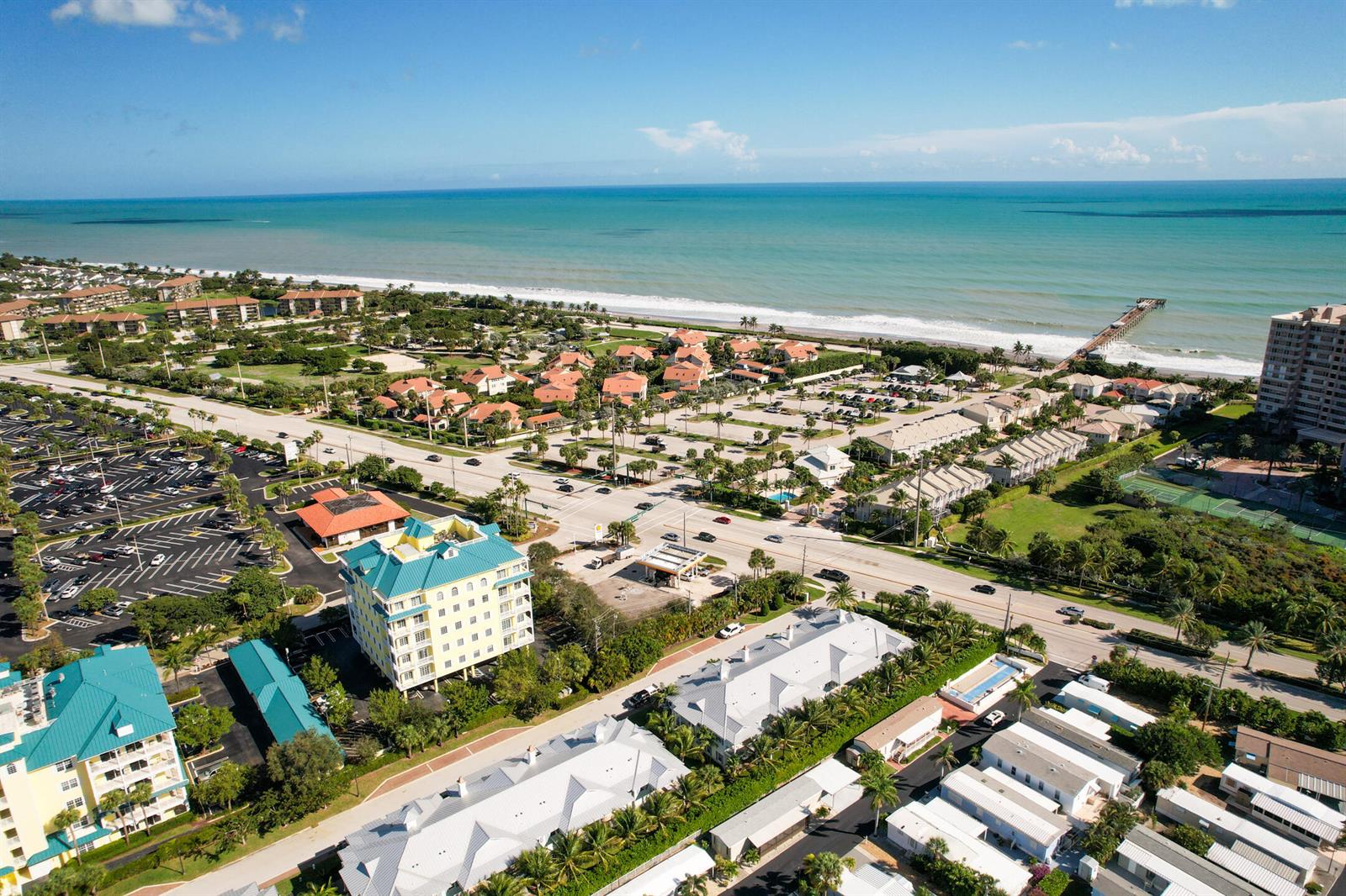 An aerial view shows a coastal community with buildings, parking lots, and a pier — 144 Ocean Breeze Drive, Juno Beach FL 33408, JUNO BEACH, FL