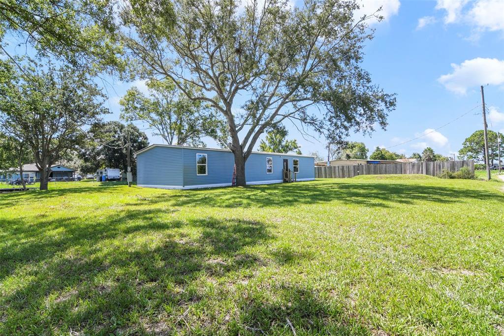 A blue manufactured home sits on a grassy lot beneath a large, mature tree — 3380 MAPLE LANE, HAINES CITY, FL