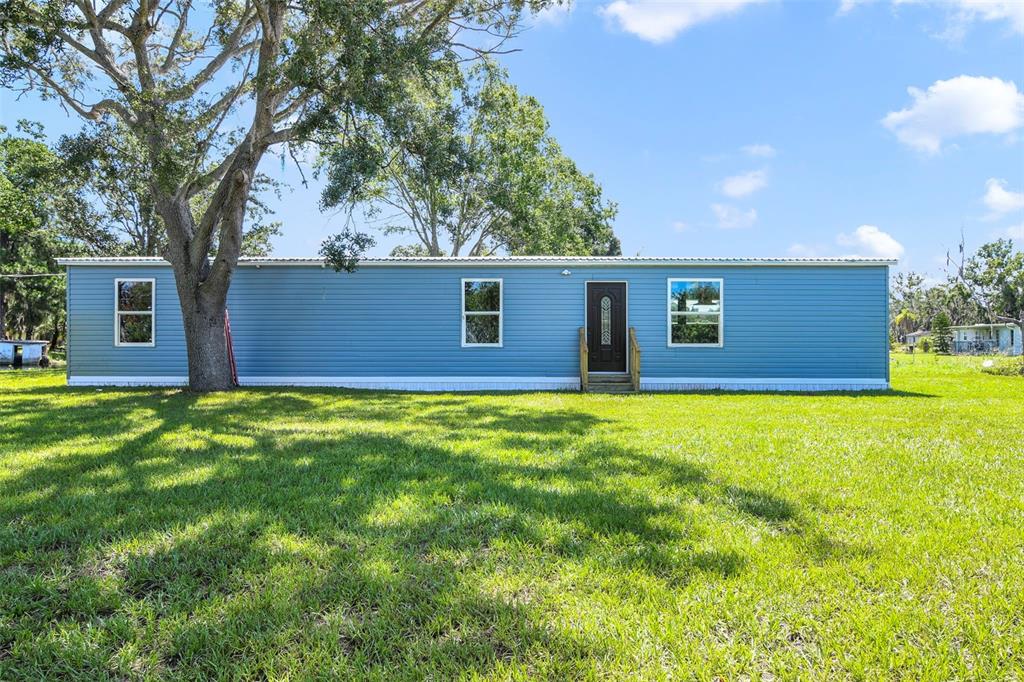 A blue single-wide manufactured home sits on a grassy lot under a large tree — 3380 MAPLE LANE, HAINES CITY, FL