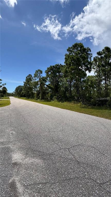 A paved road curves past a wooded lot under a blue sky with clouds — 12060 BENHAM AVENUE, PORT CHARLOTTE, FL