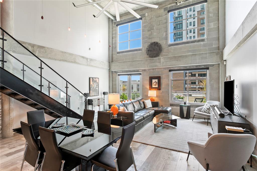 A modern two-story living and dining area features concrete walls, large windows, and a staircase — 1212 E WHITING STREET UNIT 404, TAMPA, FL