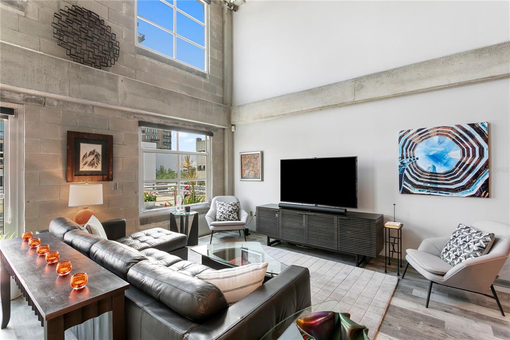 A modern living room features high ceilings, concrete block walls, and a large sectional sofa — 1212 E WHITING STREET UNIT 404, TAMPA, FL