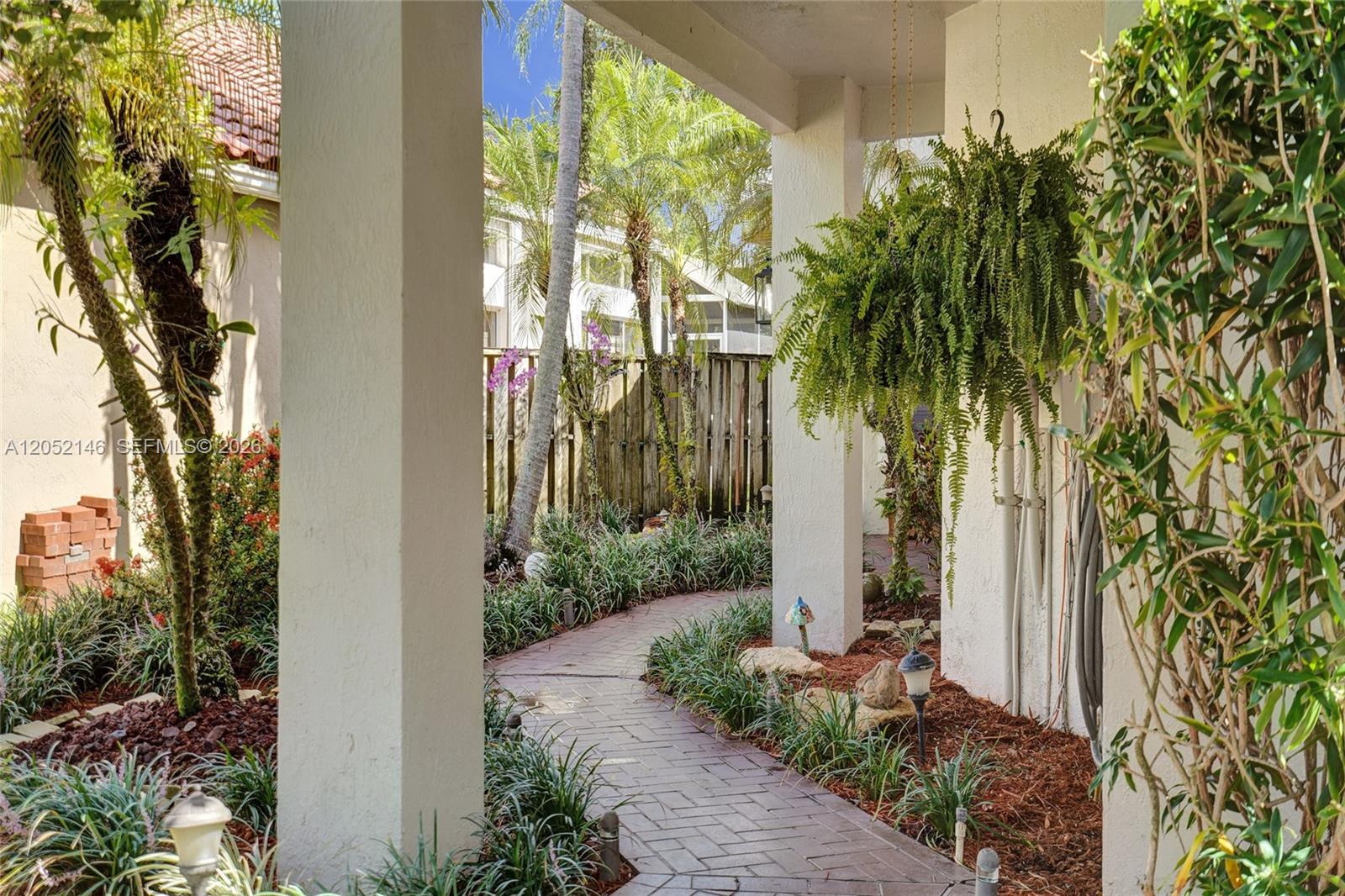 A brick walkway leads through a covered entryway with hanging ferns and lush landscaping — 10073 NW 5th St, Plantation FL 33324, PLANTATION, FL