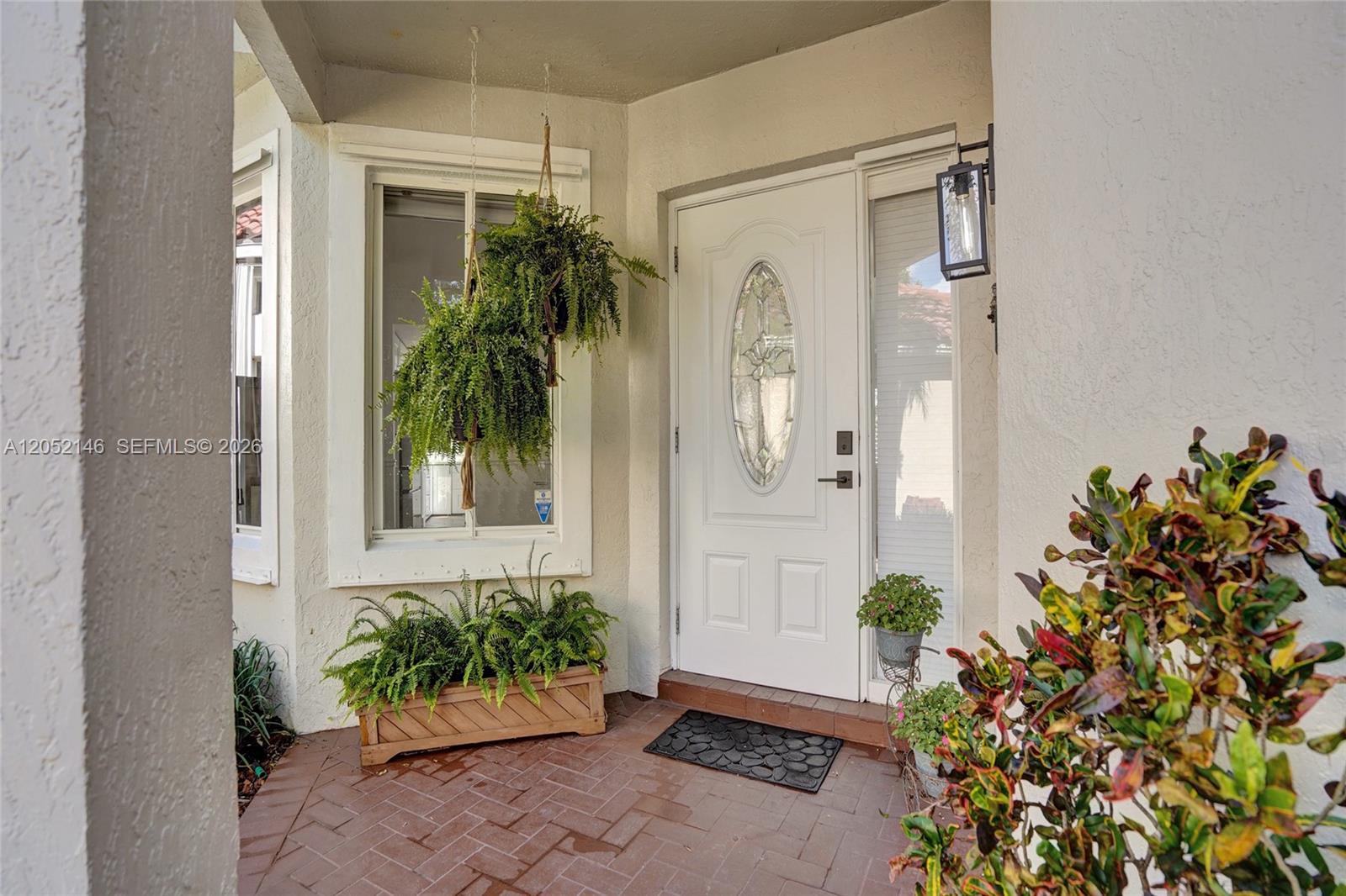 A front entryway features a white door with an oval window, hanging ferns, and brick flooring — 10073 NW 5th St, Plantation FL 33324, PLANTATION, FL