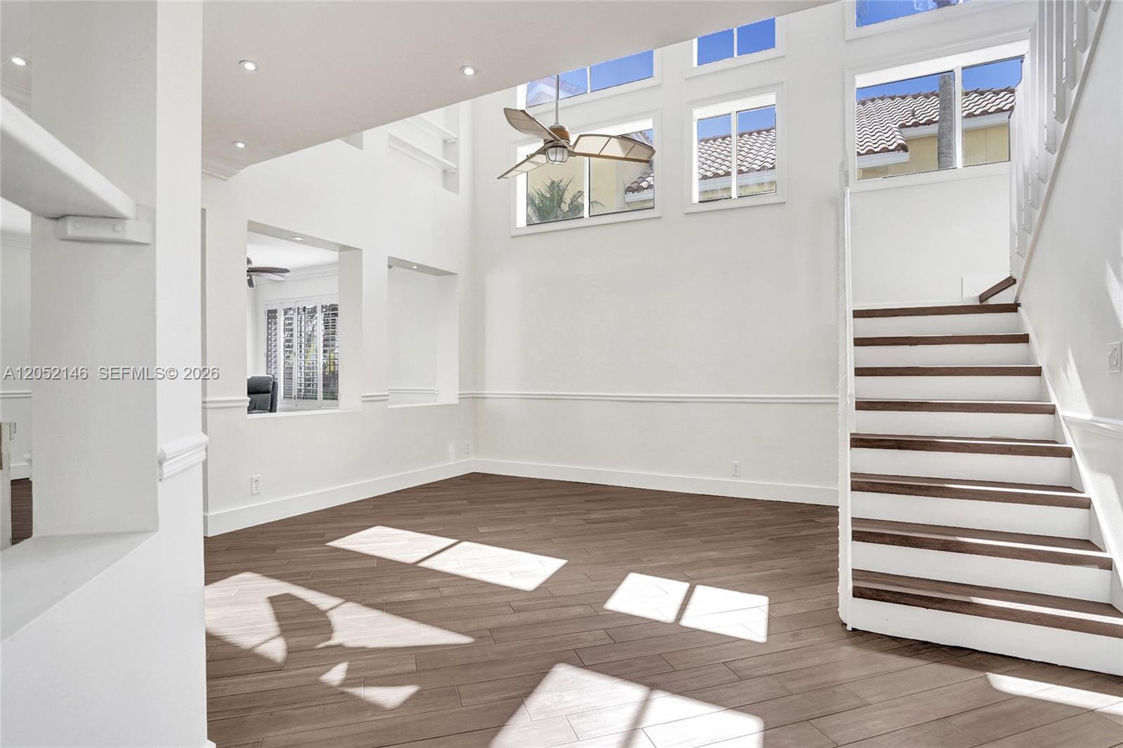 A bright, high-ceilinged living room features wood-look tile flooring, a staircase, and large windows — 10073 NW 5th St, Plantation FL 33324, PLANTATION, FL