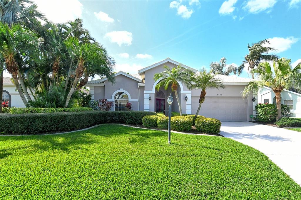 A single-story house with a beige exterior, a two-car garage, and a manicured front lawn — 6738 PLEASANT HILL ROAD, BRADENTON, FL