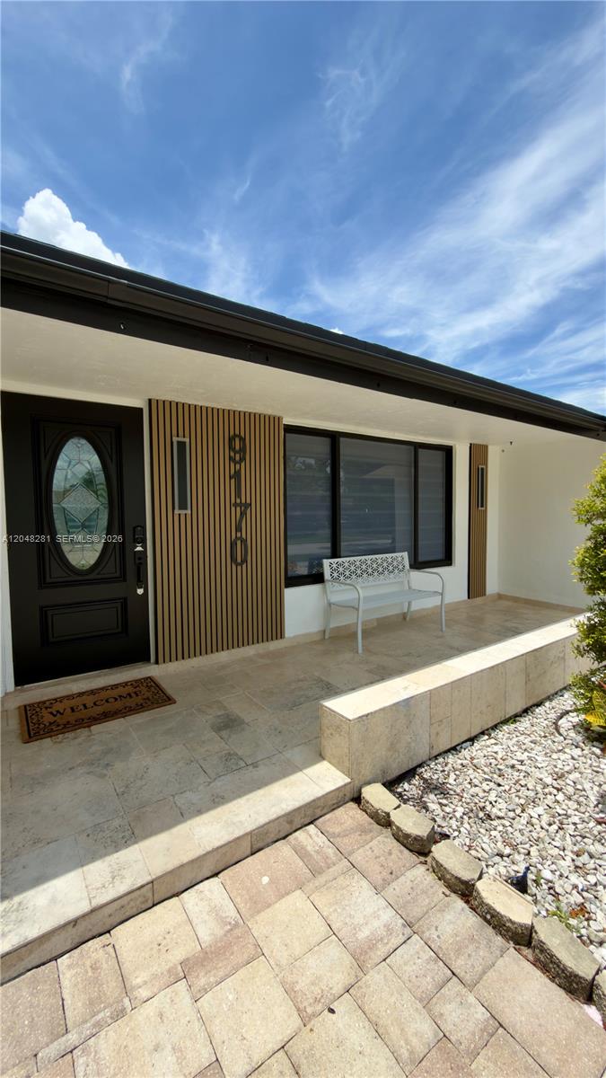 A front porch features a black door, vertical wood slats, and a white metal bench — 9170 NW 24th Pl, Sunrise FL 33322, SUNRISE, FL
