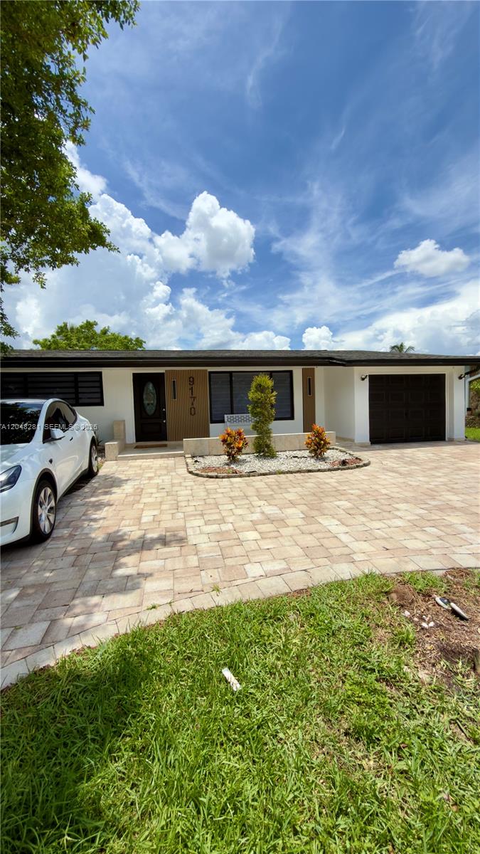 A single-story house with a white exterior, dark garage door, and a paved driveway — 9170 NW 24th Pl, Sunrise FL 33322, SUNRISE, FL