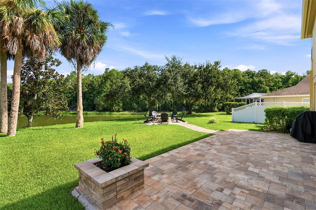 A paved patio overlooks a grassy backyard with a fire pit area and a pond — 2734 SILVERMOSS DRIVE, WESLEY CHAPEL, FL