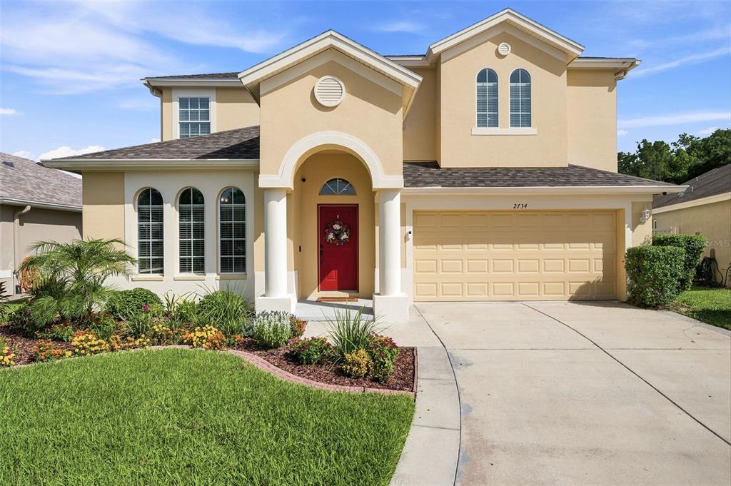 A two-story house with a tan stucco exterior, a red front door, and a garage — 2734 SILVERMOSS DRIVE, WESLEY CHAPEL, FL