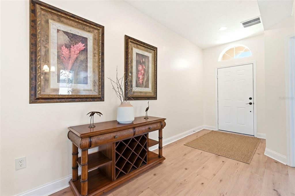 An entryway features light wood flooring, a wooden console table, and two framed floral pictures — 2734 SILVERMOSS DRIVE, WESLEY CHAPEL, FL