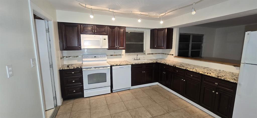 A kitchen features dark wood cabinets, granite countertops, white appliances, and tile flooring — 239 ANNAPOLIS LANE, ROTONDA WEST, FL