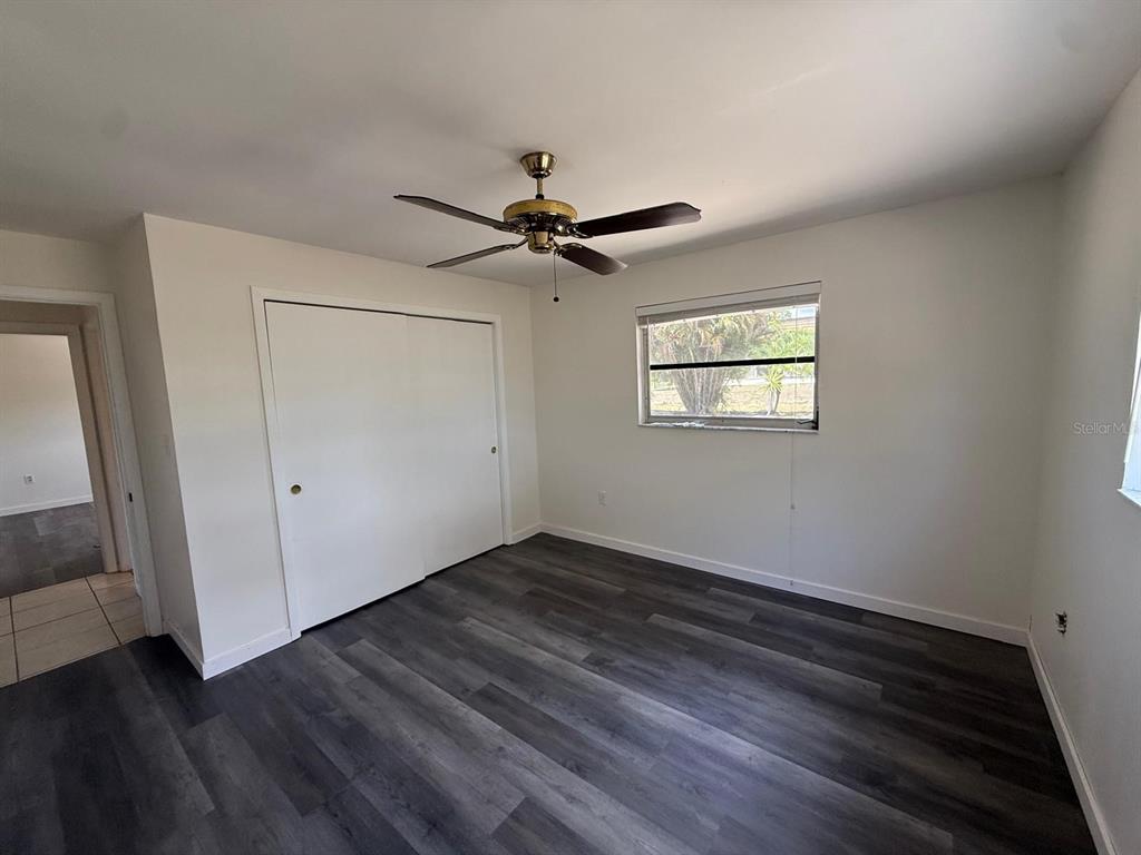 A bedroom features dark wood-look flooring, white walls, a ceiling fan, and a sliding closet — 239 ANNAPOLIS LANE, ROTONDA WEST, FL