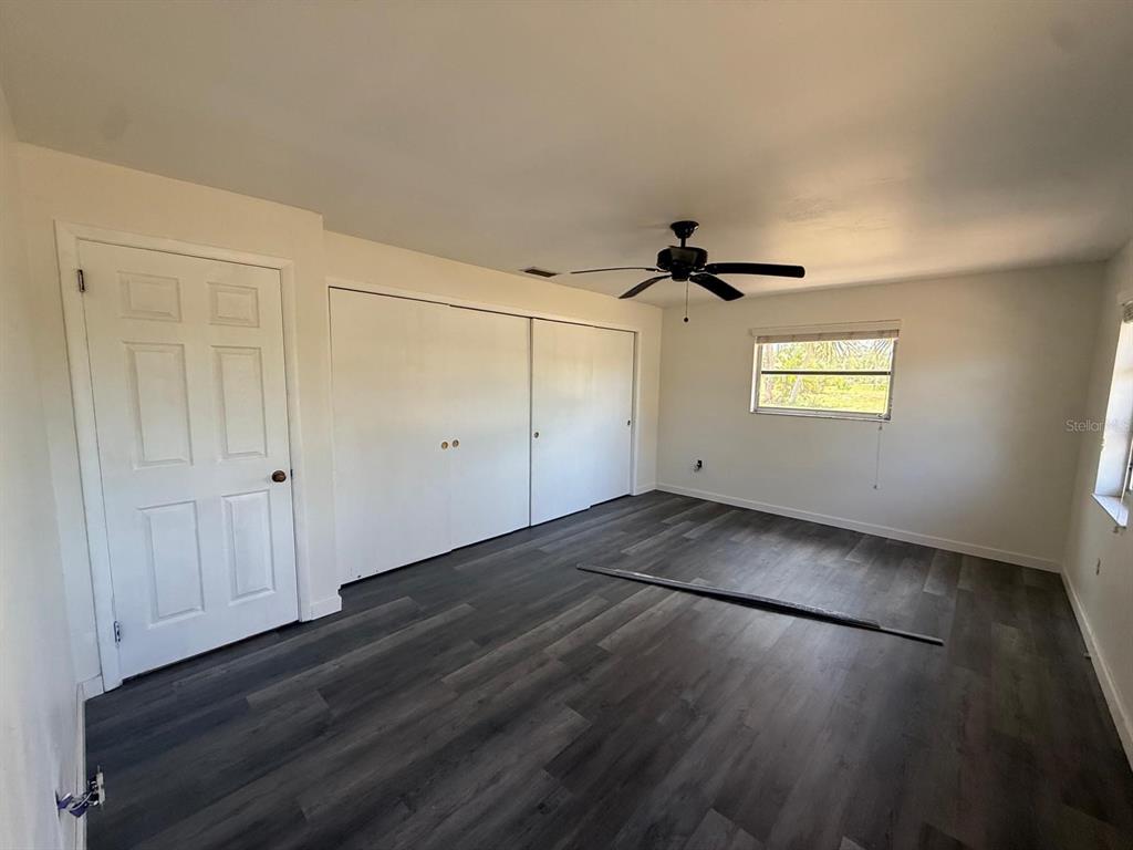 An empty bedroom features dark wood-look flooring, white walls, a ceiling fan, and sliding closet doors — 239 ANNAPOLIS LANE, ROTONDA WEST, FL