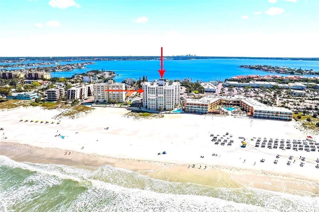 An aerial view shows a white multi-story building situated on a sandy beach — 4950 GULF BOULEVARD UNIT 807, ST PETE BEACH, FL