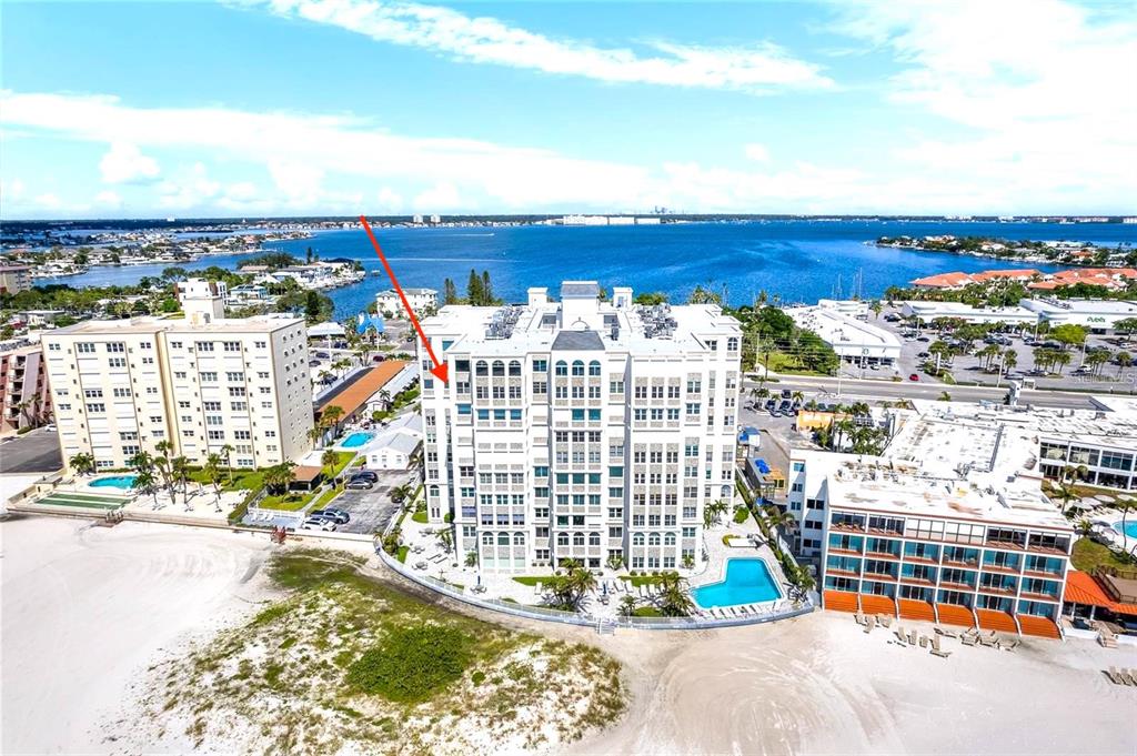 An aerial view shows a multi-story white residential building situated on a sandy beach — 4950 GULF BOULEVARD UNIT 807, ST PETE BEACH, FL