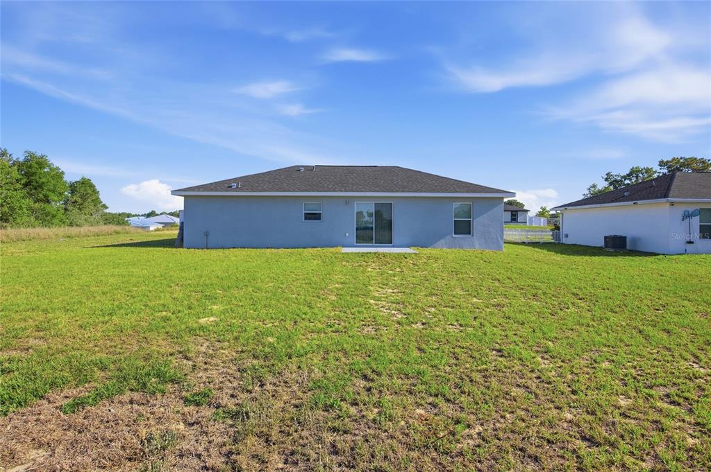 The exterior rear view of a single-story house with a lawn and sliding glass doors — 14960 SW 33RD LANE, OCALA, FL