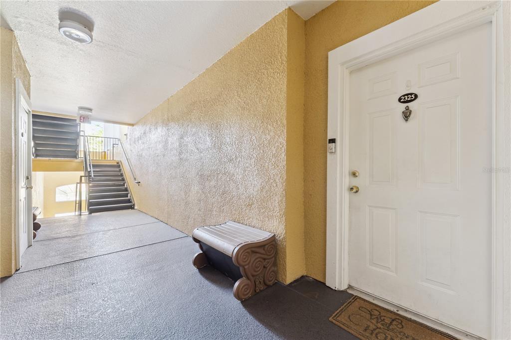An outdoor apartment hallway features a textured yellow wall, a white door, and stairs — 3751 CONROY ROAD UNIT 2325, ORLANDO, FL