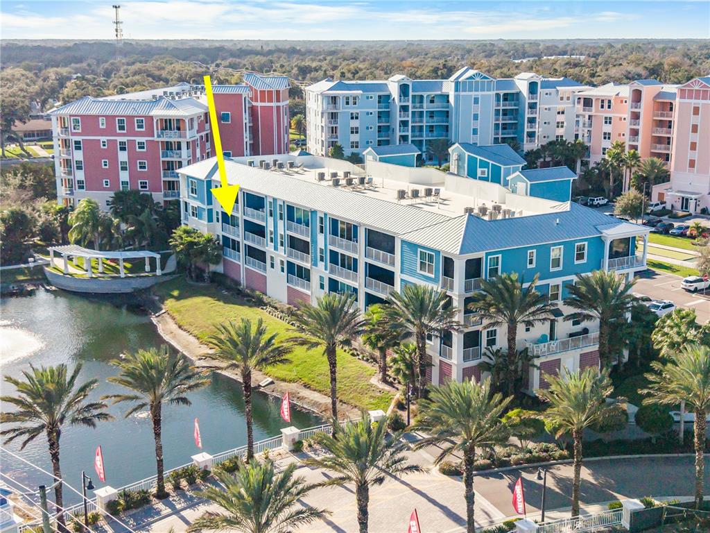 An aerial view shows a multi-story blue and white apartment building beside a pond — 1 RIVERWALK DRIVE UNIT 306, NEW SMYRNA BEACH, FL