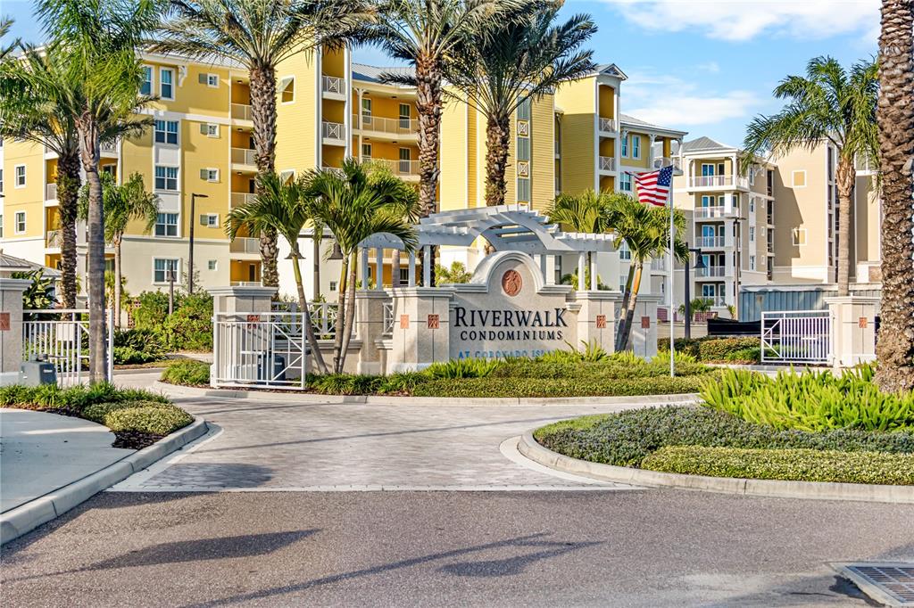 The entrance to Riverwalk Condominiums features a stone monument sign, palm trees, and yellow buildings — 1 RIVERWALK DRIVE UNIT 306, NEW SMYRNA BEACH, FL