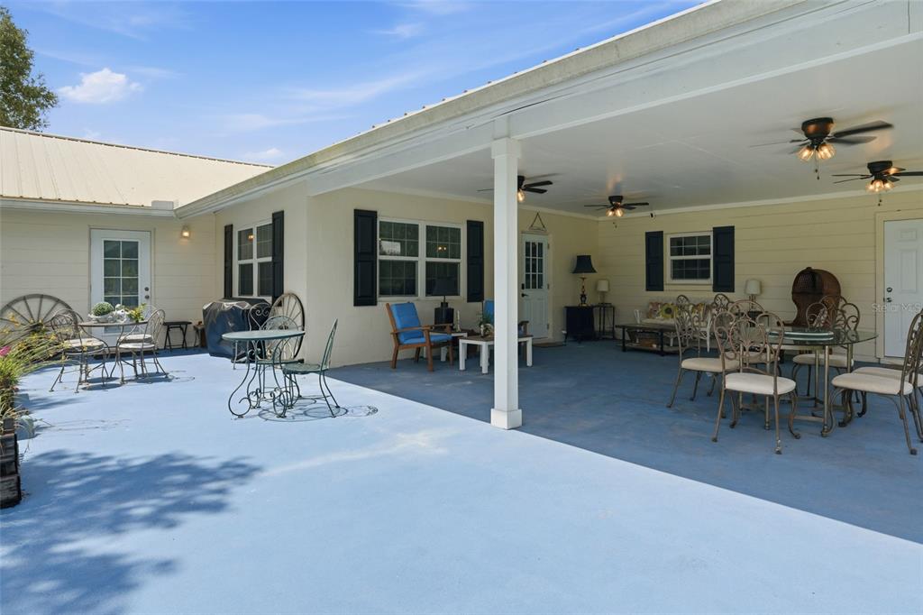A spacious covered patio features blue concrete flooring, outdoor furniture, and multiple ceiling fans — 6902 JOHNSTON ROAD, ZOLFO SPRINGS, FL