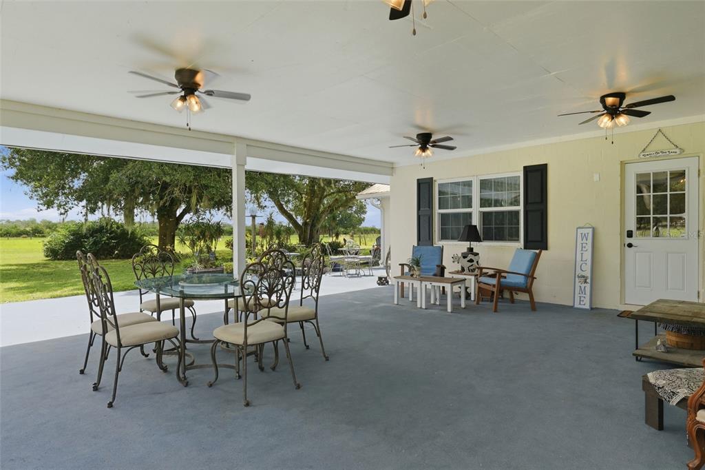 A covered patio features a dining set, lounge chairs, ceiling fans, and a view of trees — 6902 JOHNSTON ROAD, ZOLFO SPRINGS, FL