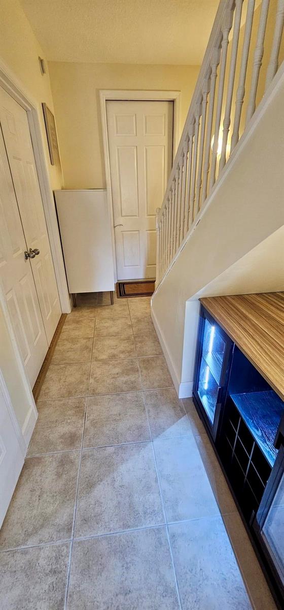 A tiled hallway features a staircase with white railings and a built-in cabinet — 146 Moorings Drive, Lantana FL 33462, LANTANA, FL