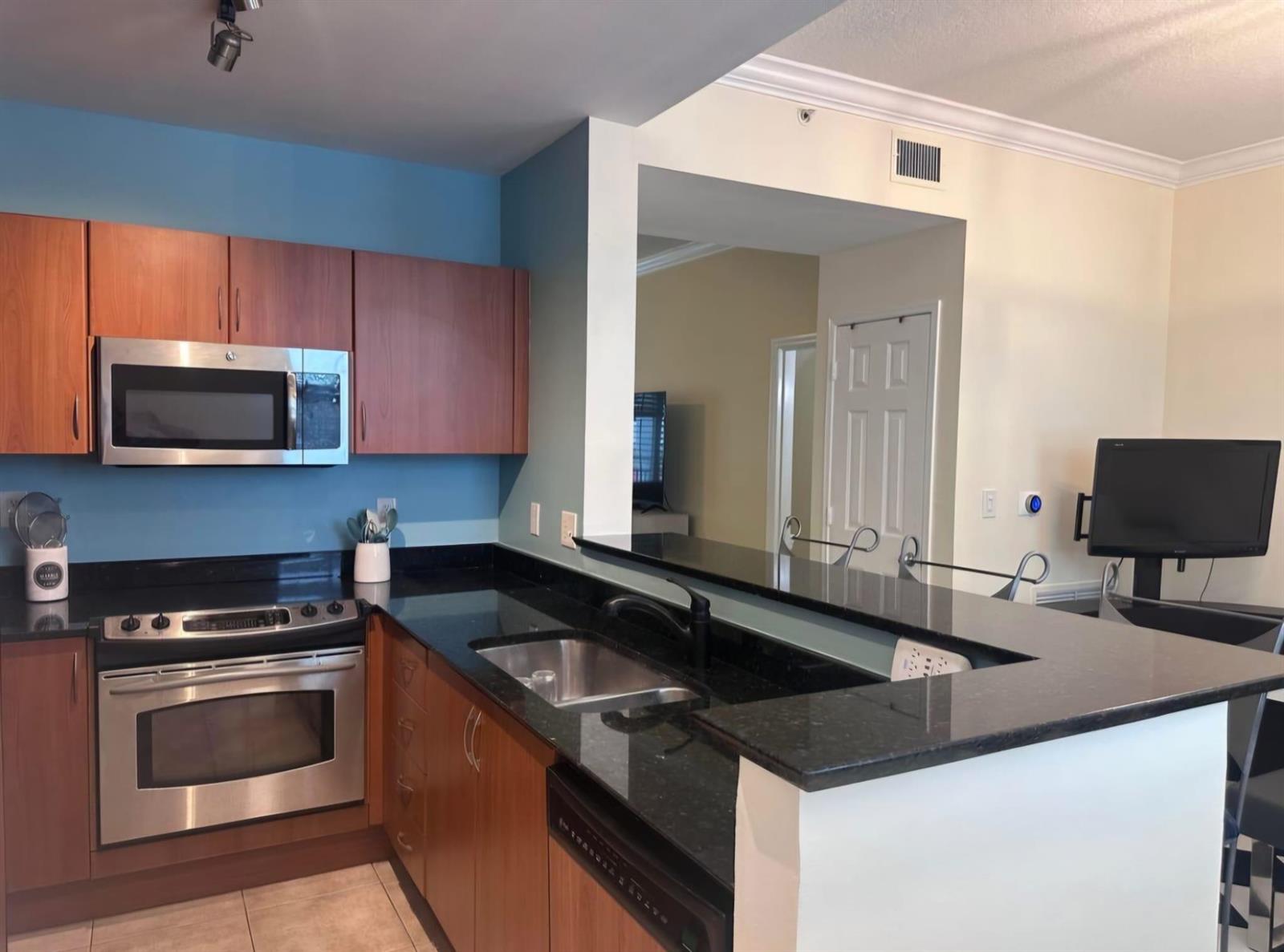 A kitchen features wood cabinets, black countertops, stainless steel appliances, and a blue accent wall — 146 Moorings Drive, Lantana FL 33462, LANTANA, FL